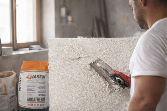 Person applying plaster to a wall with a jar of Qisen plaster in the foreground.