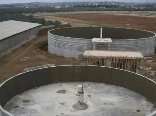 Large circular cholding tanks in the foreground, set against a rural landscape.