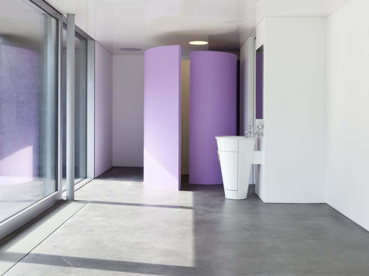 commercial bathroom with matte microcement floors, white walls and a purple stall