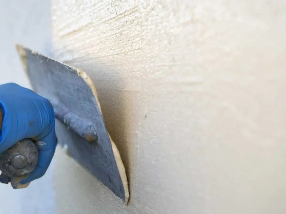 Hand using a trowel to apply or smooth Decork on a wall.