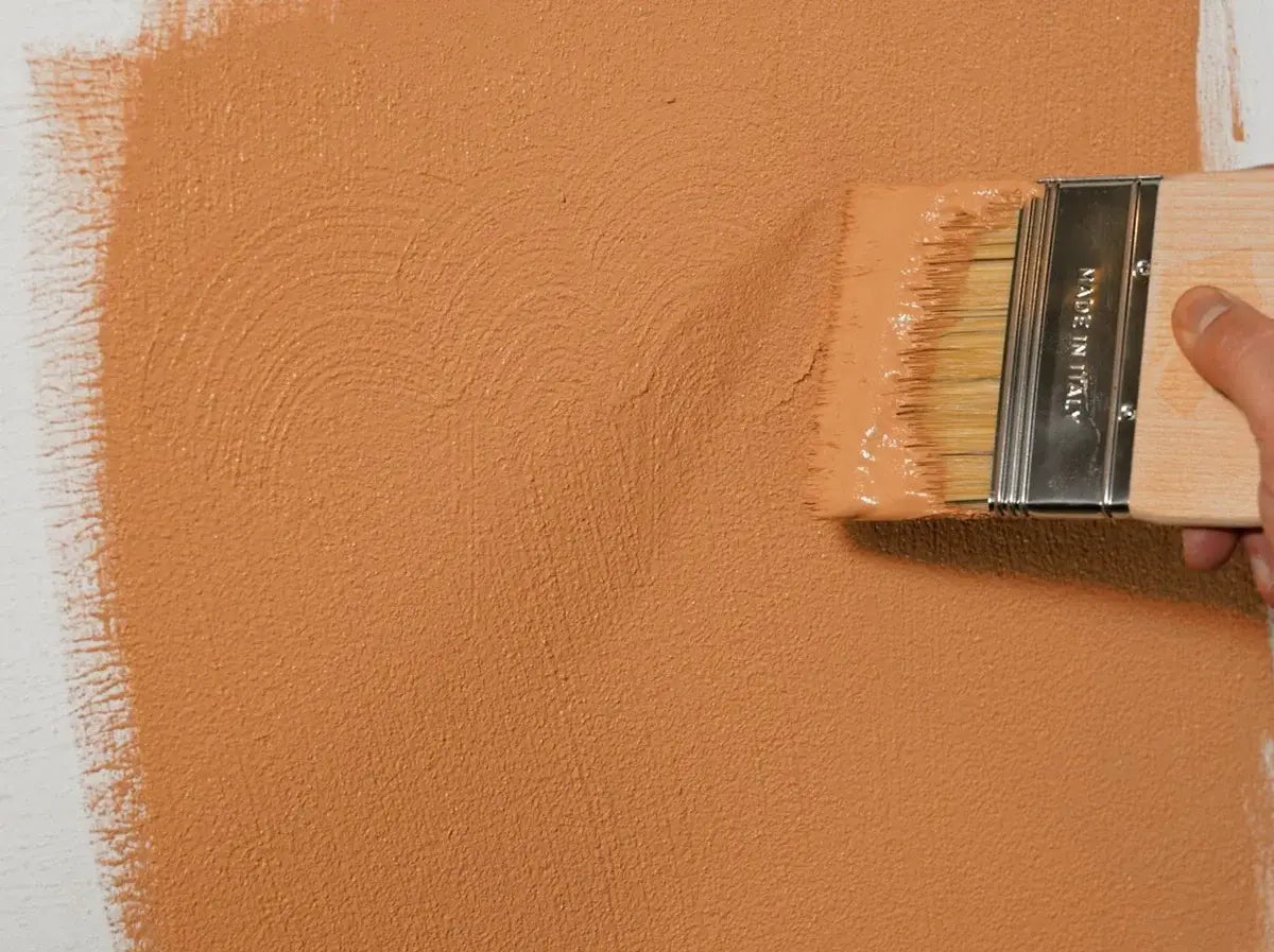 Person painting a wall with a brush in a warm orange color