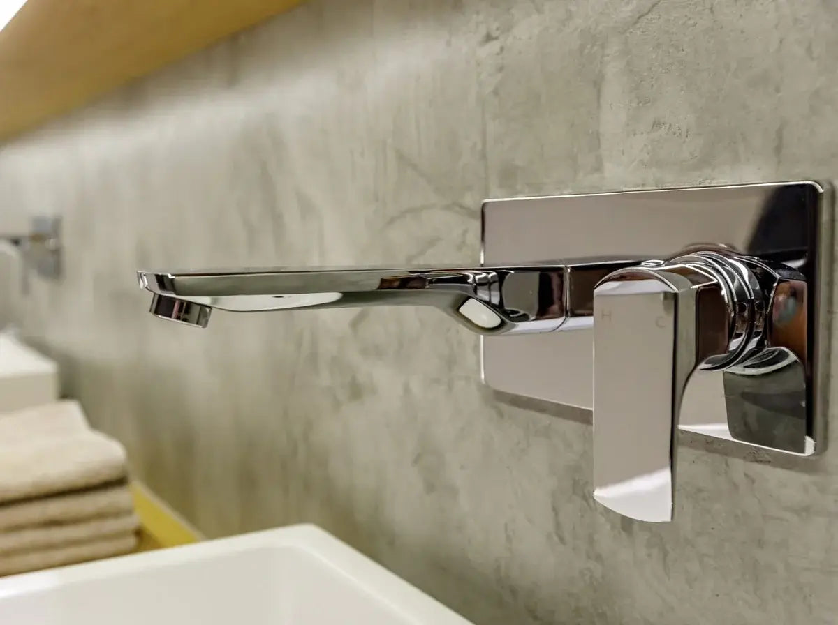 Chrome bathroom faucet mounted on a microcement wall