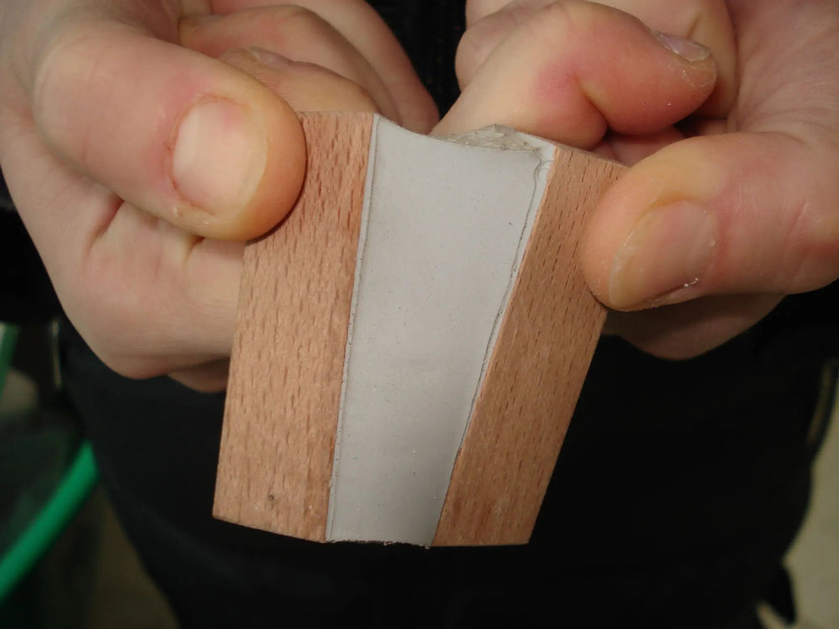 A close-up image of a hand holding a piece of wood with a bead of polyurethane sealant applied to it.