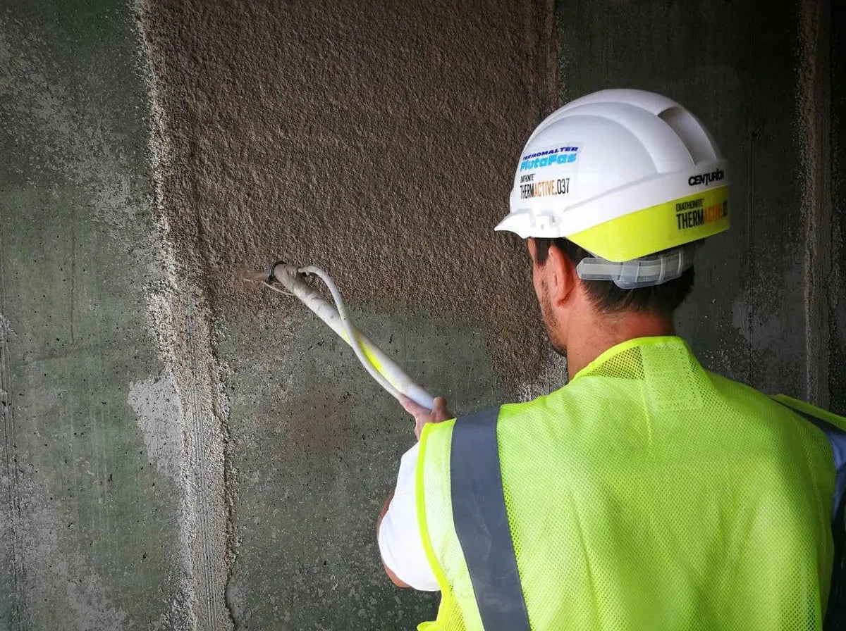 Person in high-visibility vest and hard hat applying plaster to a wall.