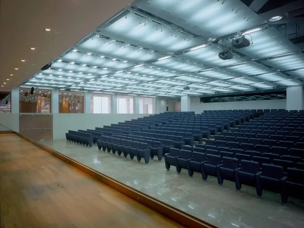 Large auditorium with rows of blue seats under a glass ceiling.