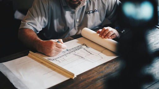 A man works on a piece of architectural paper, drawing a design.