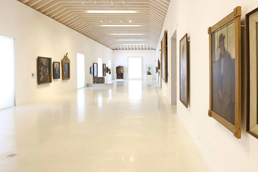A sleek art gallery corridor with paintings on both sides and a modern ceiling with exposed rafters.